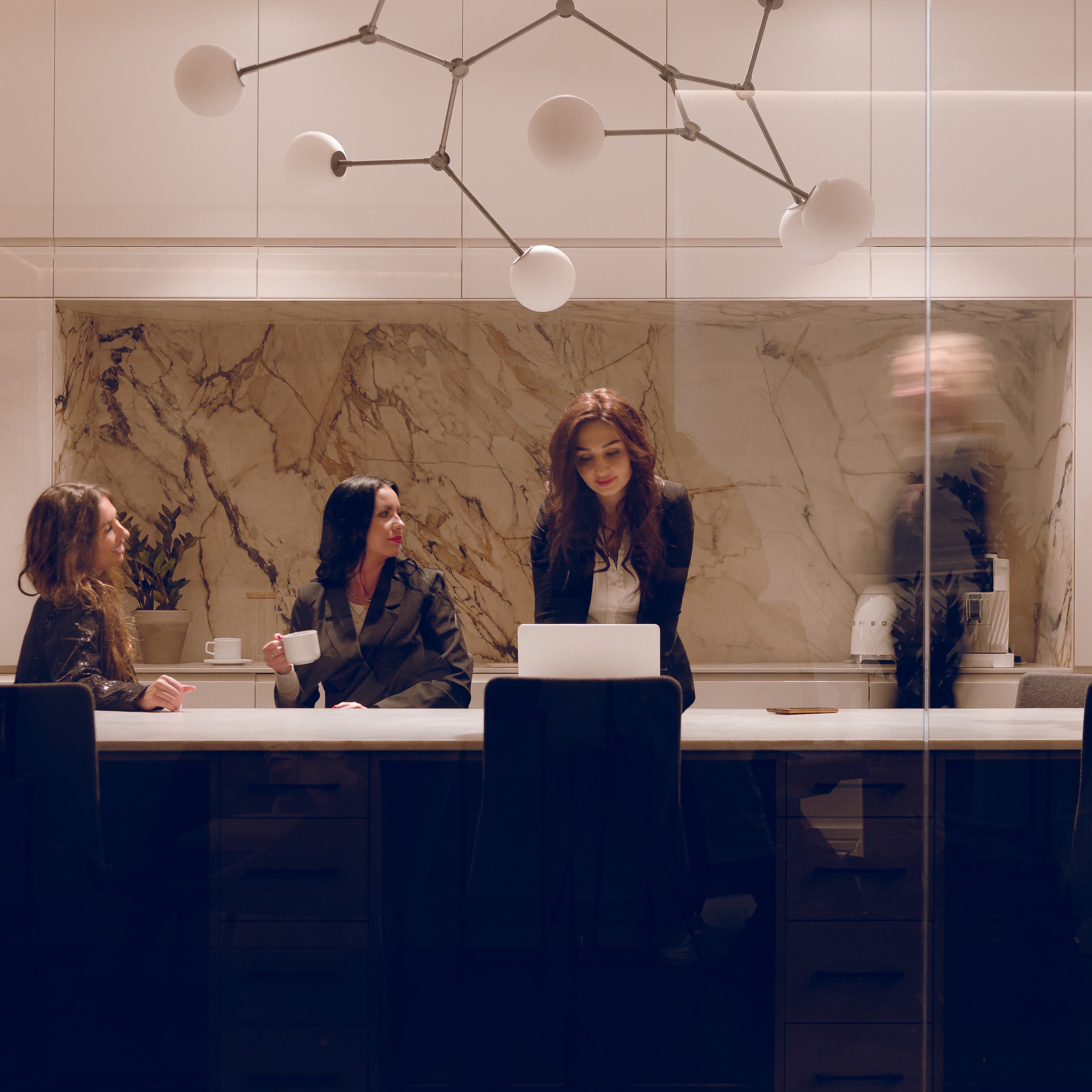 Three women having a discussion during a meeting at a long table.