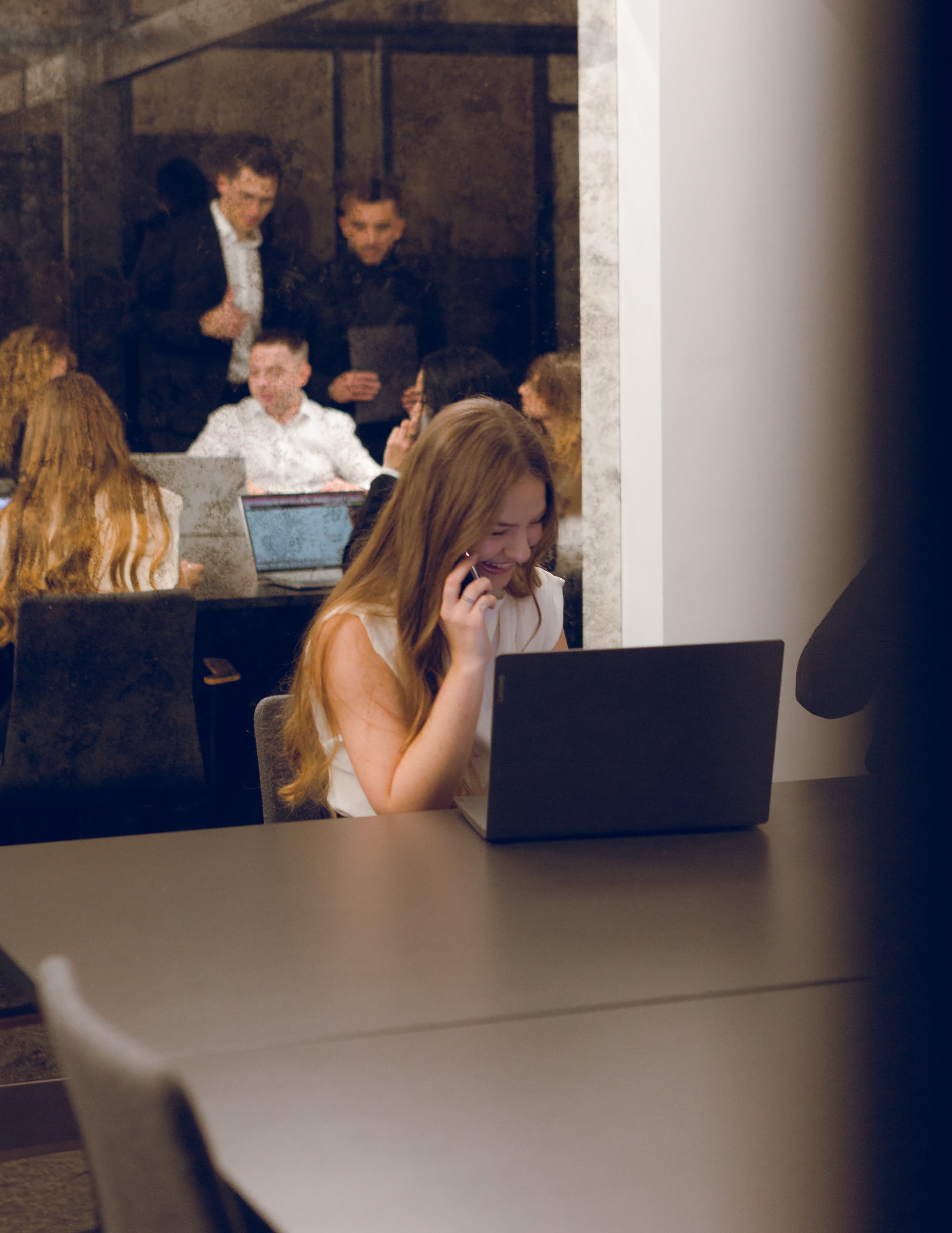 A woman talks on the phone and works on a laptop in a busy office.